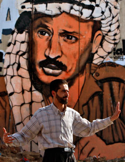 فلسطيني يقف أمام صورة لعرفات ويوجه السير في نقطة تفتيش قلنديا بين القدس المحتلة ورام الله أمس (محمد محيسن - أ ب)