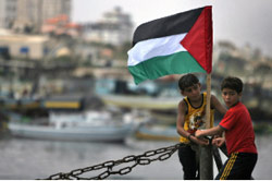فلسطينيان يعلقان علم بلادهما، على مركب صيد على شاطئ غزة أمس ( محمود همس - ا ف ب )
