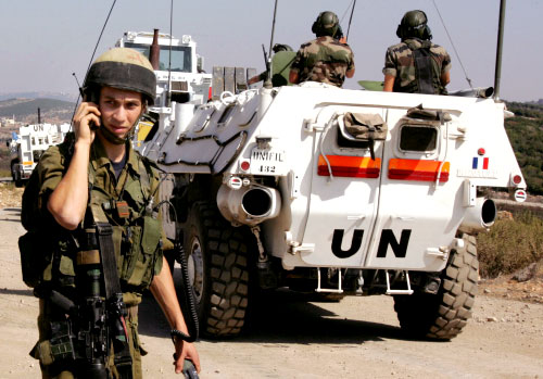 جندي إسرائلي يتحدّث إلى جهازه بالقرب من مروحين... وتبدو في الصورة آلية تابعة لـ“اليونيفيل” (أ ب)